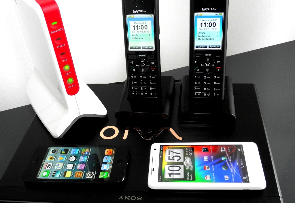 Die neue AVM Fritzbox LTE (links) holt sich das Internet via LTE 800, 1800 und 2600 aus der Luft und verteilt es hausintern per DECT an die Schnurlos-Telefone (hinten rechts) und per WLAN an Laptops wie den Sony Vaio S13A (unten) oder an WLAN-Smartphones wie das Apple iPhone 5 (links vorne) oder das weiße HTC Velocity 4G (Foto: Harald Karcher).<br><br><a href=\"http://www.zdnet.de/88142004/das-neue-lte-flaggschiff-avm-fritzbox-6842/\" target=\"_extern\">Zum vollständigen Artikel</a>